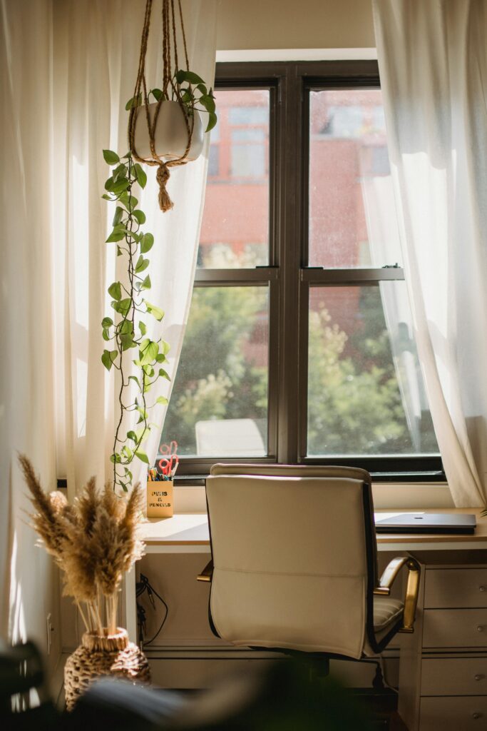 15 Neutral Office Decor Ideas That Feel Calm, Curated, and Intentional neutral office workspace with large window, soft curtains, wooden desk, and warm daylight